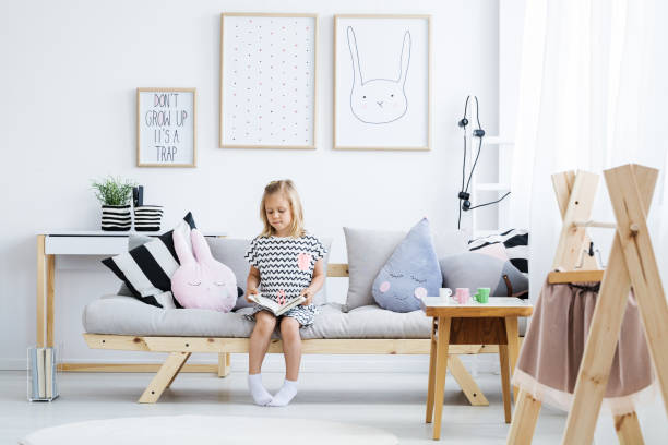 Girl reading on sofa Cute young girl reading book on stylish sofa in white room coathanger photos stock pictures, royalty-free photos & images