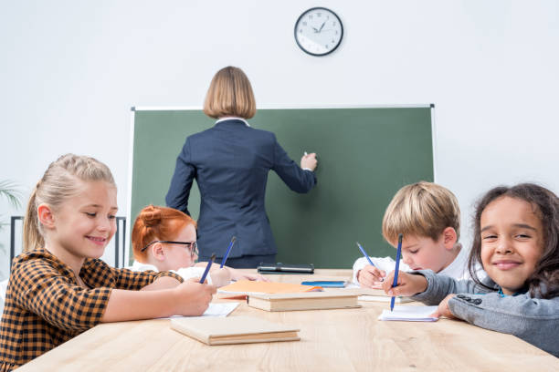 istock back view of teacher writing on chalkboard while students studying in classroom 834601076