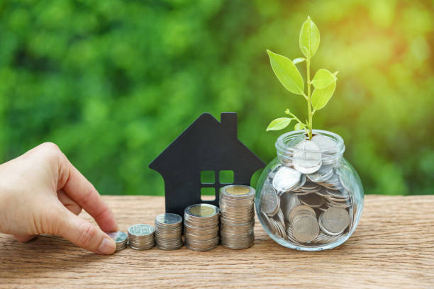 growth sprout plant in jar with full of coins and hand holding stack of coins with paper house as property or mortgage investment concept stock photo