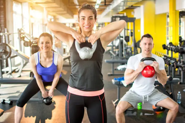 Photo of Fit friends working out together with kettle bells in gym.