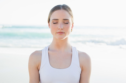Calm young woman sitting on the beach with closed eyes