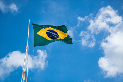 The national flag of Brazil with fabric texture waving in the wind on a blue sky. 3D Illustration