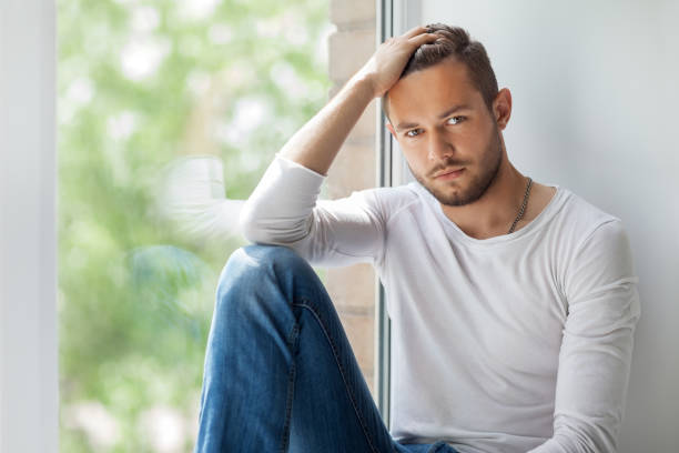 istock Handsome thoughtful man touching his hair relaxing on window sill 834653126