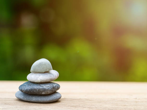 istock Four stones stacked placed on a wooden board. The backdrop is black on green. 834672462