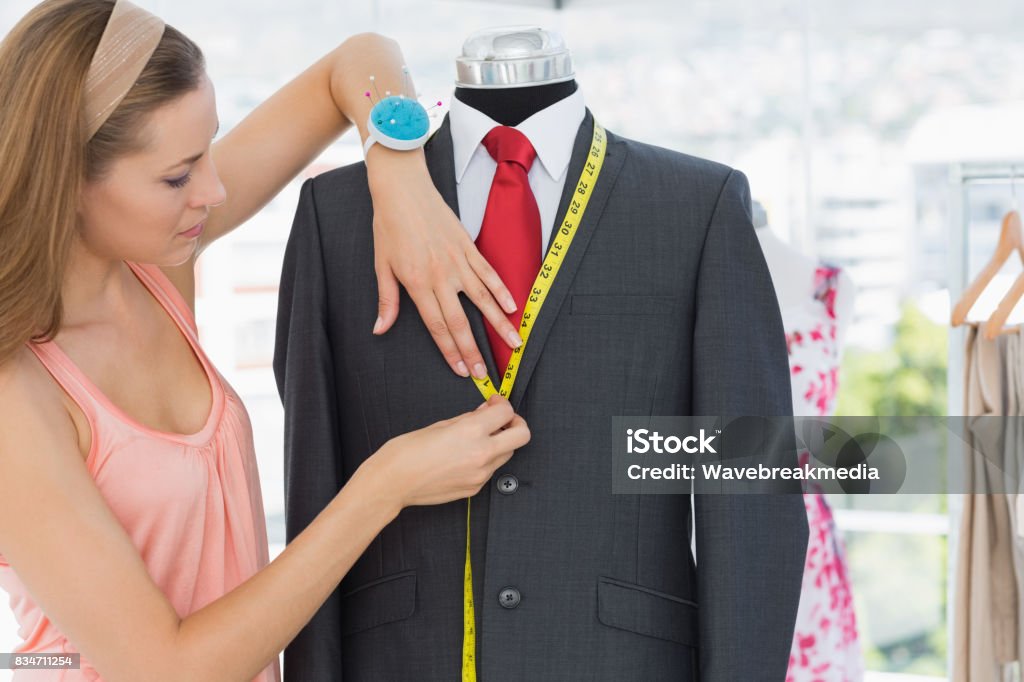 Female fashion designer measuring suit on dummy Side view of a female fashion designer measuring suit on dummy at office 30-34 Years Stock Photo