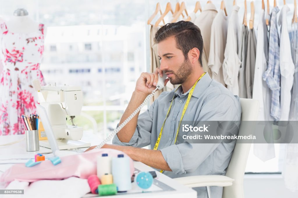 Young male fashion designer using phone Side view of a young male fashion designer using phone in the studio 20-29 Years Stock Photo