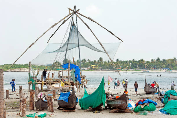 Chinese fishing nets and local fishing boats, Fort Kochi, Cochin, Kerala, Southern India. Chinese fishing nets and local fishermen, Fort Kochi, Cochin, Kerala, Southern India. Chinese fishing nets form the backdrop to this rural scene by the waters edge, whilst local fishermen tend their nets having unloaded their catch from fishing boats on the shore in the foreground, Fort Kochi, Cochin, Kerala, Southern India cochin kerala india chinese fishing net stock pictures, royalty-free photos & images