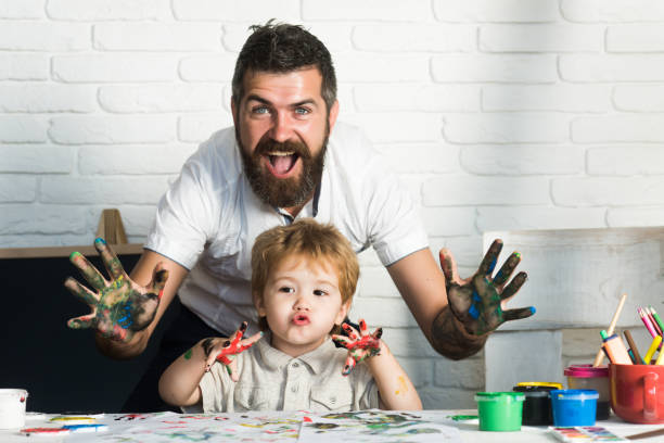 joy family art, padre e figlio felici si mostrano le mani in colori vivaci, dipingono insieme immagini, arte per tutta la famiglia, allegro insegnante di disegno. educazione a domicilio con i genitori. buona infanzia. mani in vernice - uomo dipinge foto e immagini stock