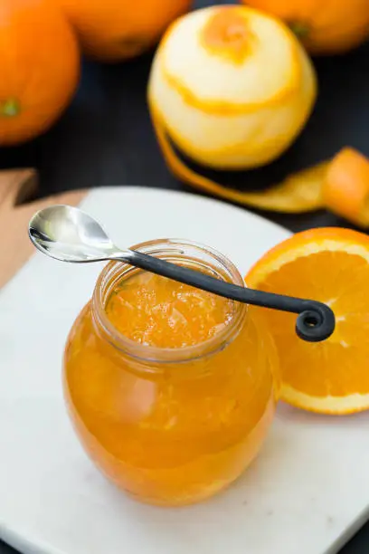 Jar filled with orange jam with orange on the background. Rustic spoon.