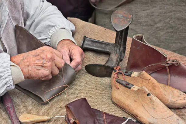 elderly shoemaker makes artisan shoes on an old bench with old tools for leather working