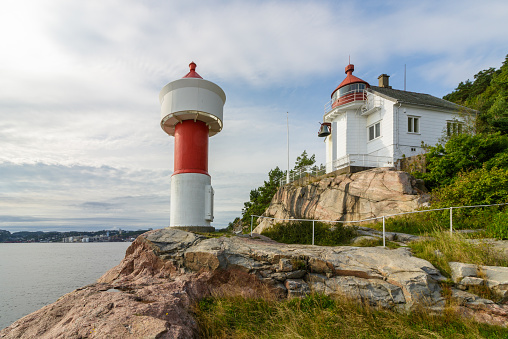 The Lighthouse at Odderoya in Kristiansand, Norway. Blue sky and white clouds over the ocean in summer