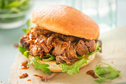 Pulled pork sweet bun with mixed lettuce leaves on blue background
