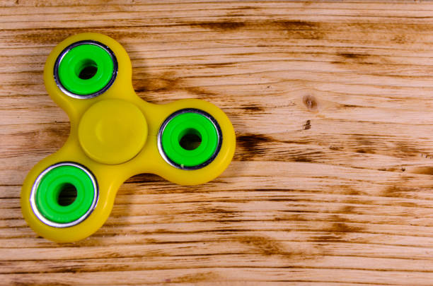 istock Yellow fidget spinner on wooden desk. Top view 834788928