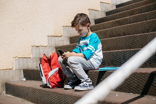 Child sitting outside school and playing games on his cell phone