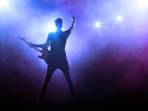 Male young adult jumping and playing an electric guitar isolated on white background