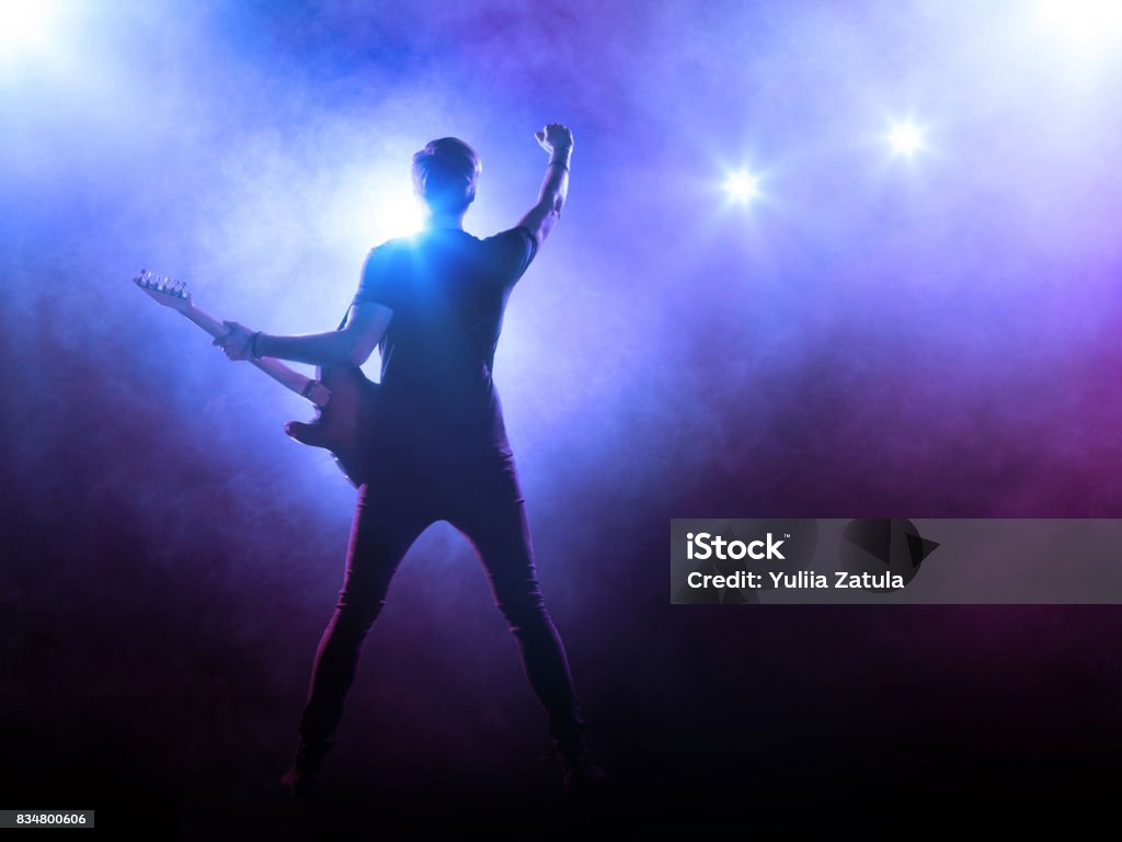 Guitarist performing on stage Silhouette of guitar player on stage on blue background with smoke and spotlights Rock Musician Stock Photo