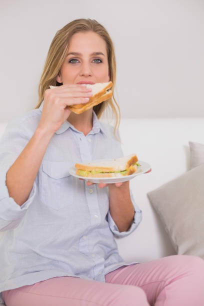 istock Happy casual blonde sitting on couch eating sandwich 834836054