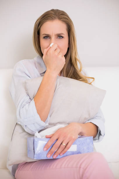 istock Frowning casual blonde sitting on couch blowing nose 834837554