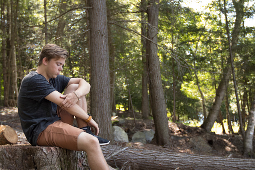 Young man sitting outdoors in wooded area and praying