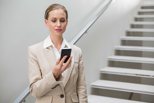 Thoughtful stylish businesswoman holding smartphone standing on stairs