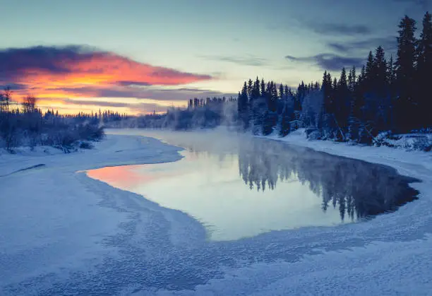 Chena River in Fairbanks, sunset clouds and trees reflected in glass-like ice