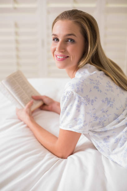istock Natural happy woman lying on bed holding book 834906400