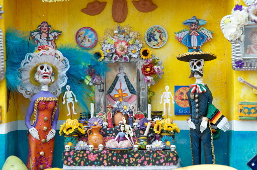 Sanctuary in honor of the dead in vibrant colors, with shades of yellow and blue, to celebrate the day of the dead in Mexico. Perhaps the most serious emblem of the holiday is the Offrenda, an altar honoring the dead. Offrendas are most often created in honor of one’s ancestors or loved ones, and contain a number of traditional elements, many drawn from indigenous Mexican traditions: Crosses and other religious emblems, including statuettes of saints. Water, sacred to indigenous pre-Columbian cultures, and a symbol of baptism and new life in the Catholic church. Salt, a preservative and purifying agent. Copal, a native incense used by the Aztecs. Candles, whose light guides the dead. Flowers, particularly the Cempazúchitl, or flower of the dead- the marigold, sacred to Mictlantecuhtli, the Aztec god of the dead, they guide the spirits to their altars using their vibrant colors and scent, they also represent the fragility of life. 