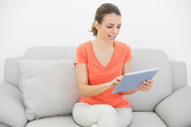 istock Happy young woman working with her tablet sitting on couch 834987590