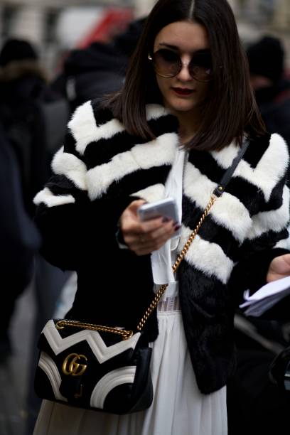 A young walking wearing a black and white outfit is looking at her phone. A fashionable looking lady looks down at her phone as she walks along a London street. london fashion week stock pictures, royalty-free photos & images