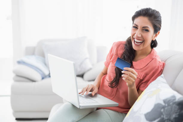 istock Laughing brunette sitting on her sofa using laptop to shop online 835066762