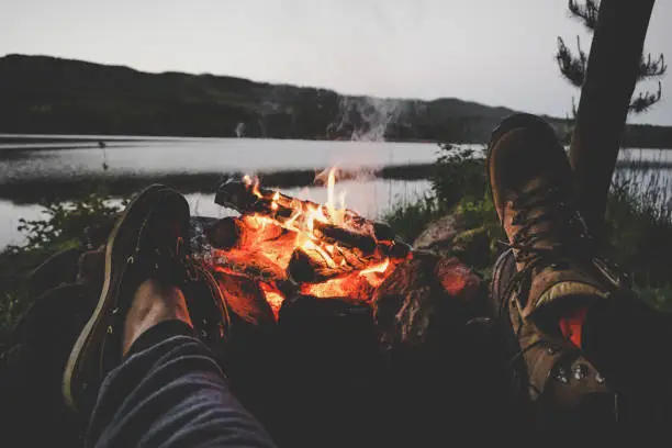 Young couple holding their feet on a fire with a lake in the background.