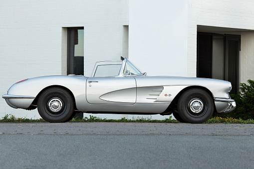 Hamburg, Germany - 08/09/2015: Close up (street shot) of a silver-gray Chevrolet Corvette C1 Oldtimer Vehicle in Hamburg on the country road. No people visible. in the background the wall of a white house can be seen.