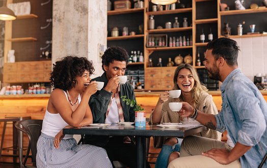 Diverse group of friends enjoying some coffee together in a restaurant and talking. Young people sitting around cafe table and drinking coffee.