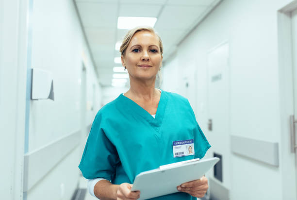 Portrait of mature female nurse working in hospital Portrait of mature female nurse working in hospital. Woman healthcare worker with clipboard in corridor. female nurse photos stock pictures, royalty-free photos & images