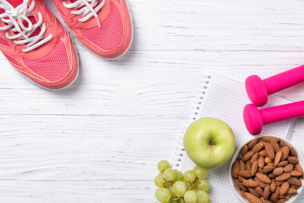 fitness und gesunde ernährung konzept, rosa turnschuhe und hanteln mit apfel, trauben und mandeln nüssen auf notepad, hölzernen hintergrund, ansicht von oben mit textfreiraum - weights dieting apple healthy eating stock-fotos und bilder