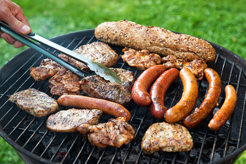 Assorted meat and sausage on grill with the coals, cooking outdoors, weekend concept
