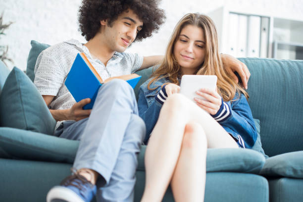 istock Young people sitting at couch with a tablet and a book 835158620