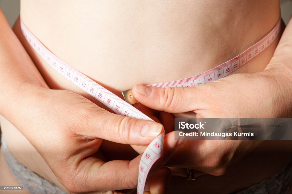 Woman measuring her waistline fat tummy Woman measuring her waist. Weight loss. Partial view close up Abdomen Stock Photo