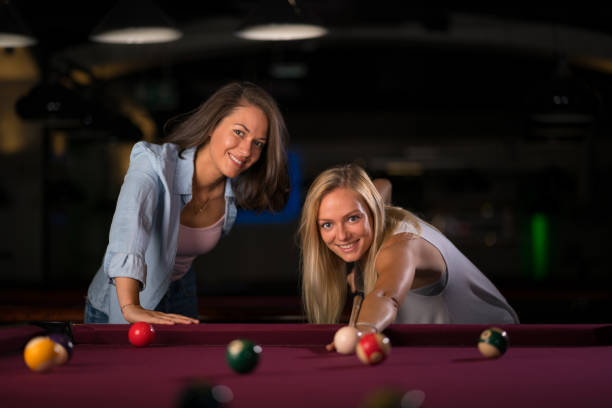 two beautiful young women playing billard smiling at camera