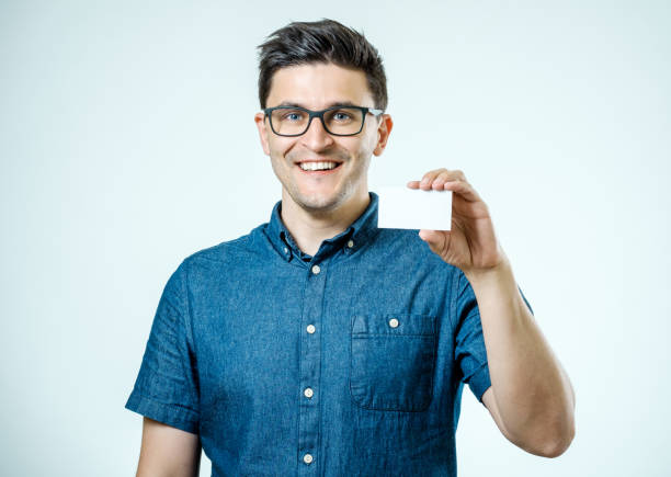 casual young businessman holding business card. isolated on gray - glasses holding business card imagens e fotografias de stock