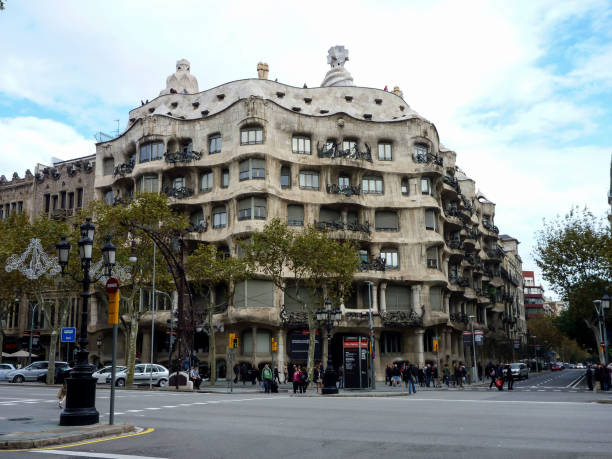 Barcelona, Cataluña, Spain - January 15, 2010: People are sitting on a stone bench under a clear blue sky, admiring Antoni Gaudí's unique gingerbread house-like lodge, an iconic example of Catalan Modernisme architecture in Barcelona