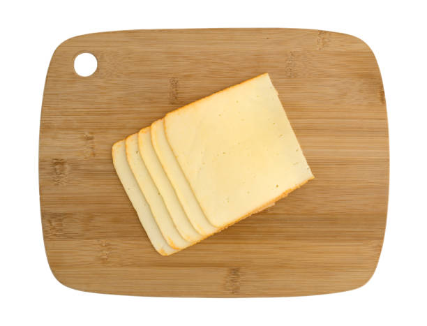 Muenster cheese slices on a wood cutting board Top view of muenster cheese slices stacked on a wood cutting board isolated on a white background. munster stock pictures, royalty-free photos & images