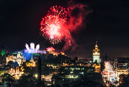 Fireworks exploding over the city of Edinburgh, photographed from Calton Hill, with the traffic of Princes Street visible towards the right.