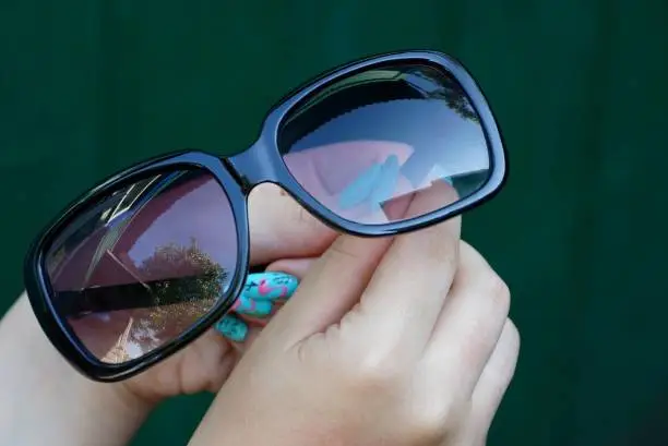 Brown transparent glasses in the hands of a girl on a green background