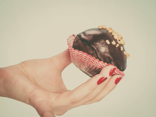 Woman holding chocolate cupcake about to bite