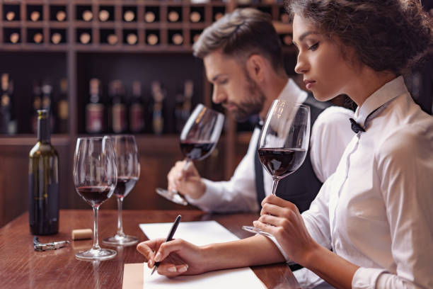 Sommeliers tasting wine in cellar Two sommeliers, male and female tasting red wine and making notes at degustation card sommelier photos stock pictures, royalty-free photos & images