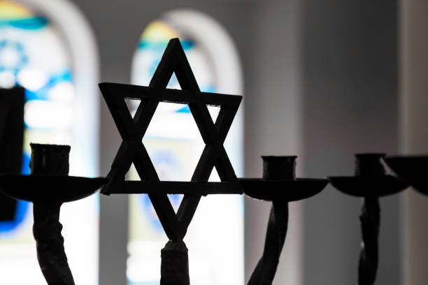Close up of Star of David silhouette inside Jewish Synagogue Close up image depicting the Jewish religious symbol of the star of David inside a synagogue. The star is in silhouette, while in the background stained glass windows are blurred out of focus. Horizontal colour image with copy space. synagogue stock pictures, royalty-free photos & images