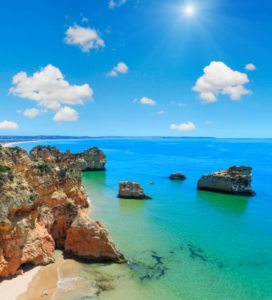 Rocks near beach Dos Tres Irmaos. Top view with blue sunshiny sky (Portimao, Alvor, Algarve, Portugal). People in boat are unrecognizable.