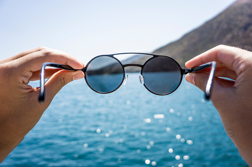 Hands holding sunglasses next to the sea