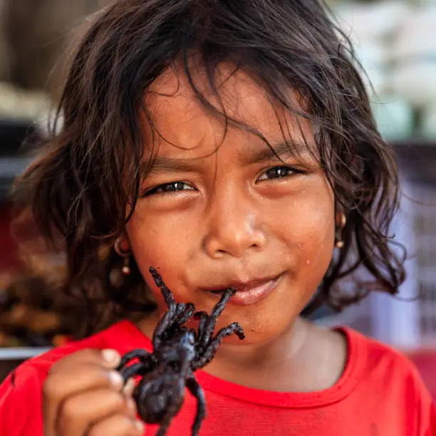 Photo of Cambodian little girl eating deep fried tarantula, street market, Cambodia